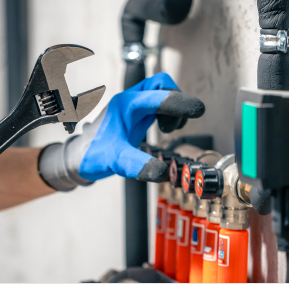 A person wearing blue gloves holds a wrench, preparing to work on a Plumbing task.