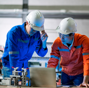 Two men in hard hats reviewing information on a laptop at a construction site.