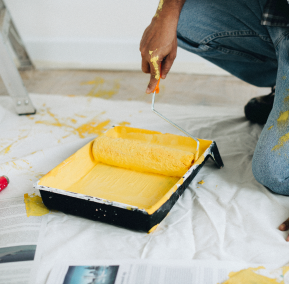 A man painting a room with bright yellow paint, focused on the wall with a paint roller in hand.
