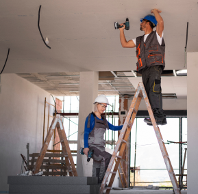 Two men installing fixtures on a ceiling in a commercial building.