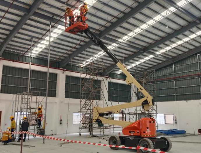 In a large warehouse, a man is focused on working with a lift, managing items at height.