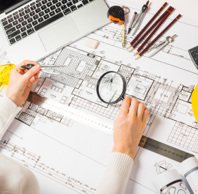 A person examines a blueprint closely with a magnifying glass, focusing on intricate details.