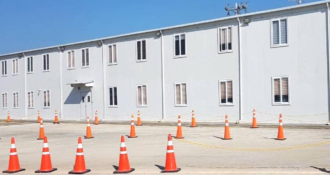 A large white building with orange traffic cones positioned in front of it, indicating a construction or maintenance area.